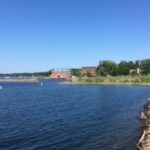 A scenic view of a calm lake with a rocky shoreline and lush green trees in the background.